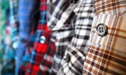 Close-up of a row of colorful plaid shirts hanging side by side. The image highlights the fabric textures and variety of checkered patterns.